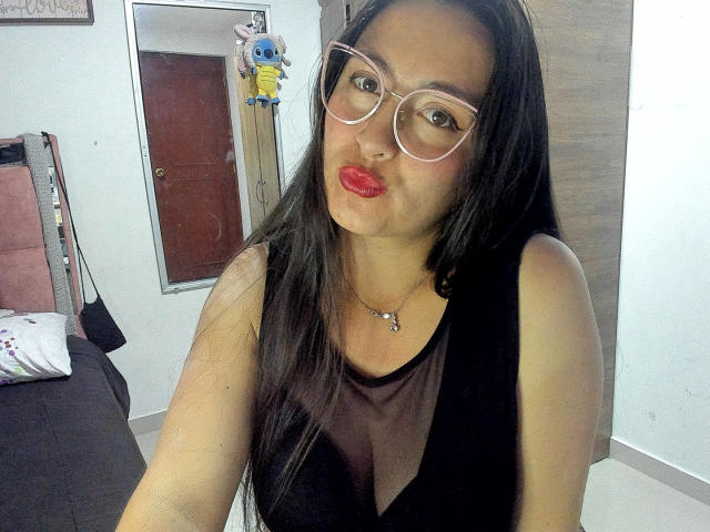 VenusSweetPalmer with long black hair, wearing a black sheer top, pink glasses, red lipstick, and a necklace, puckering her lips in a selfie. Her tits are not visible.