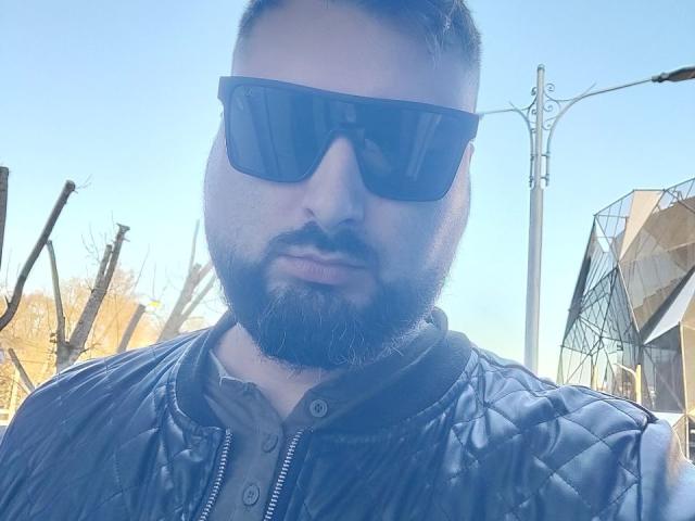 NormanGlory, a bearded dude with a black quill jacket and dark sunglasses, has a serious face and a slightly blurred, blue-tinted selfie. His nose is prominent.