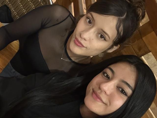 GabriellesRusso with dark hair in a bun and black sheer top, and GabriellesRusso with straight black hair, both smiling at the camera, showing cute faces and black outfits.