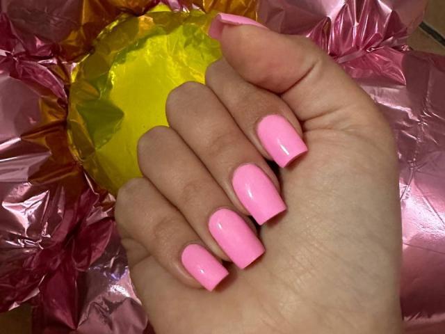 BalletSwan's hand with shiny pink nail polish, holding a yellow object against crinkled pink and yellow foil. Boobs are not visible, but her hand is in focus.