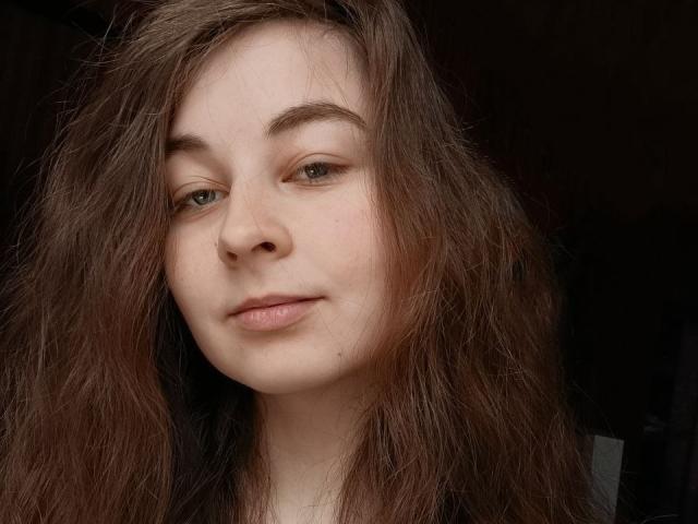 LilithDiva has long, messy brown hair, light skin, green eyes, and a small nose with a slight smile. Her tits are not visible in the image.
