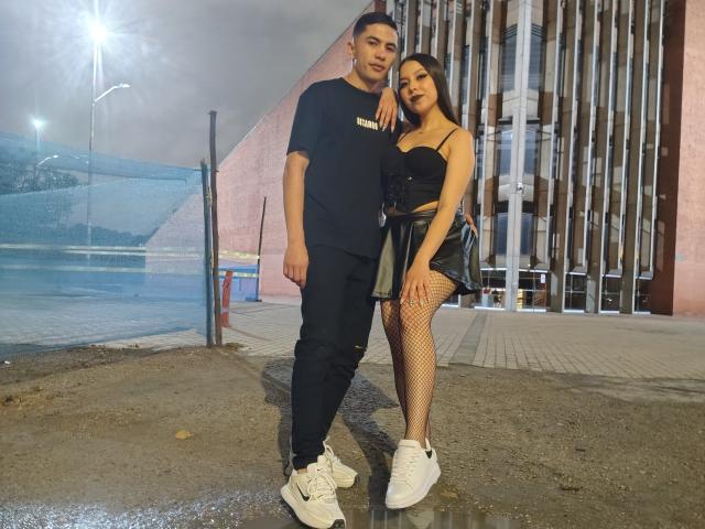 KylieAndJustin, a dude in a black tee and jeans, stands next to a chick with black tits in a strapless top, black skirt, fishnet legs, and white sneakers.