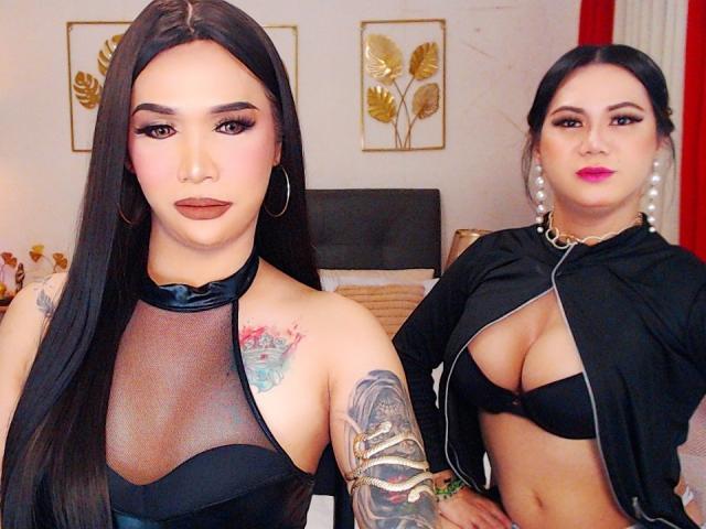 Due ragazze asiatiche con lunghi capelli neri, rossetto marrone e orecchini a cerchio, che indossano una maglietta nera trasparente che mostra i loro seni e un braccio tatuato. Un'altra ragazza asiatica con orecchini di perle, maglietta nera e grandi seni..