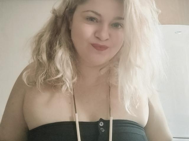 HurricaneCathrine with blonde wavy hair, fair skin, red lipstick, black strapless top showing small boobs, necklace, slightly smiling, soft light, upper body shot.