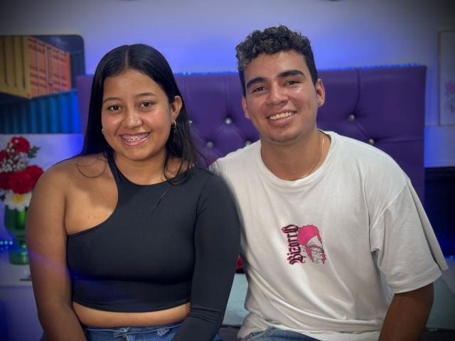 NatyAndYerry, a chubby Latina woman with black hair in a one-shoulder black top and small tits, sits next to Yerry, a curly-haired Latino man in a white tee.