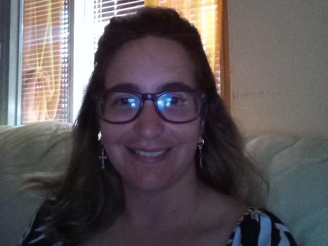 SempreVogliosa69 has glasses, a nose ring, and cross earrings, smiling with her tits slightly visible in a black and white striped top. She's sitting on a beige couch.