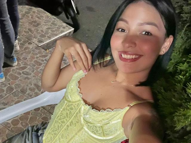 LeaJamess has small tits in a yellow lace top, smiling with dark hair, holding a white plastic tray, standing on a cobblestone path at night.
