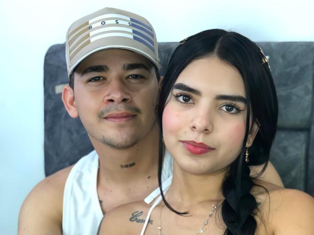 LauraAndKevin und Kevin liegen eng beieinander, tragen ein weißes Tanktop und eine gestreifte Mütze. LauraAndKevin hat ihr geflochtenes Haar und trägt Make-up..
