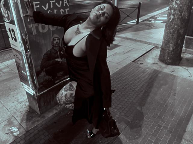 Chili se penche contre un arrêt de bus, haut tiré vers le bas, seins énormes, streetwear sombre, graffiti, nuit, trottoir humide, ombragé.