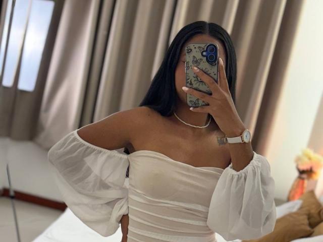 AnaRome with long black hair, wearing a white off-shoulder dress with puffy sleeves, holding a phone covering her face, showing her tits and a wristwatch.