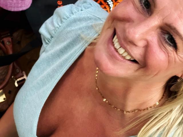 Blueberry-10-hot with a big smile, showing off her tits in a low-cut, light blue shirt, wearing a gold necklace, and blonde hair, in a selfie.