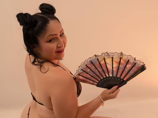 ArabelaFoxy with black hair in buns, wearing a black lace bra, holding a colorful fan, looking over her shoulder, smiling, showing her back and butt.