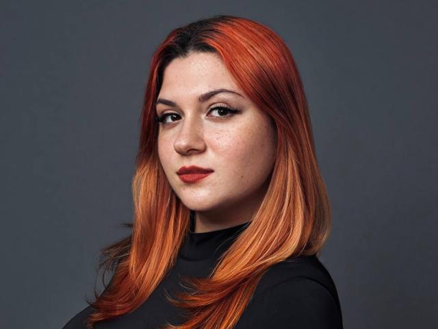 CrimsonDusk has red-orange hair, fair skin with freckles, dark eyeliner, red lipstick, and is wearing a black top. She's looking at the camera with a slight smile.