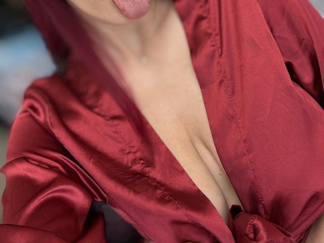 La robe rouge en satin de Rosalyn, avec un décolleté en V plongeant qui révèle sa poitrine, sa langue légèrement sortie, sa peau claire visible, la texture lisse et brillante du tissu, et de subtils plis..