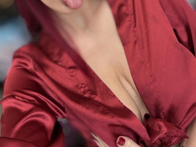 Rosalyn, con la lengua afuera, vestida con una bata de satén rojo, que revela su escote. Su bata está atada, mostrando su piel desnuda y sus uñas rojas..