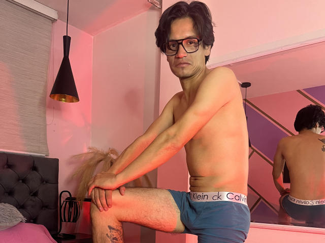 ThonixMr. is a slim, shirtless dude with glasses, black wavy hair, and blue Calvin Klein underwear, sitting on a bed with a reflective mirror behind him.