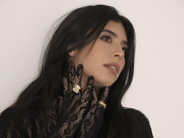 MiluSky has black hair, wearing black lace gloves with gold buttons, and a black lace top. She's looking to the side with a slight smile, showing a gold earring.