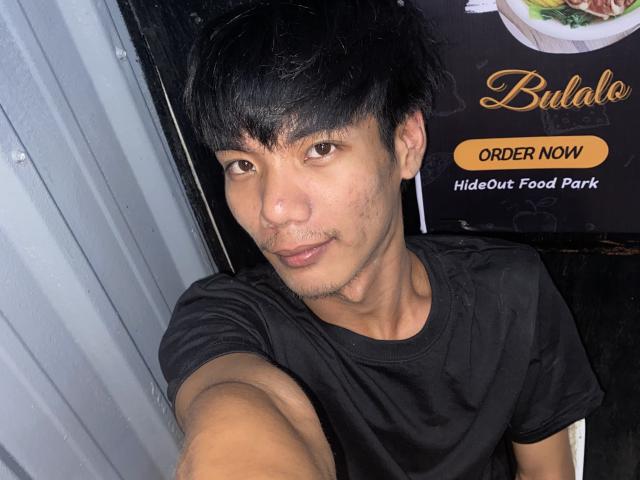 BiMonsterCock with short black hair, light brown skin, small goatee, and wearing a black shirt, taking a selfie, showing a slight smile, in a dimly lit room.