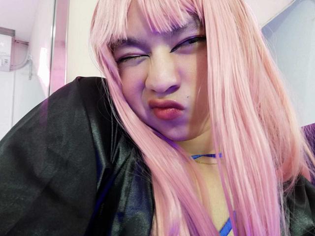 OliverPelman with pink hair, black shirt, blue choker, pouty lips, and half-closed eyes, looking cute and slightly annoyed, with a visible mole on the left cheek.