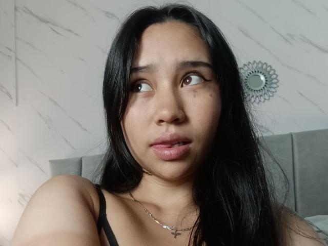 Karollteyes a de longs cheveux noirs, des yeux marrons et une légère moue. Elle porte un haut noir à bretelles et un collier. Ses fesses ne sont pas visibles..