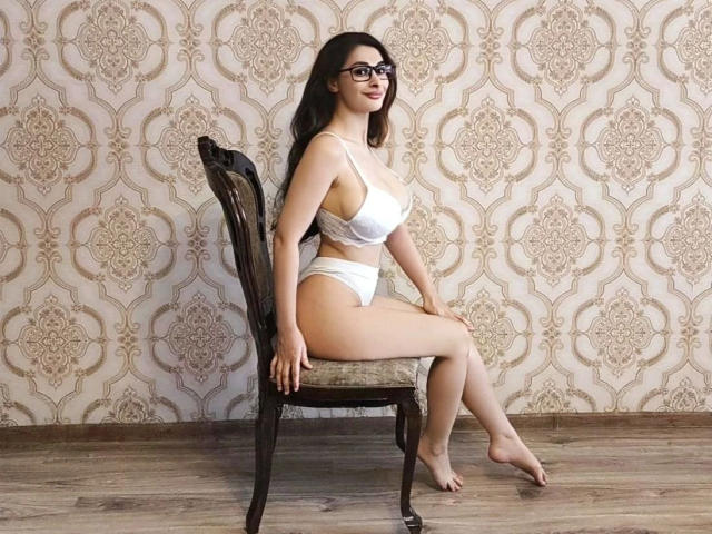 HeisseNathalia-hot with glasses, white bra, and panties, sitting on an ornate chair, showing her tits and ass, barefoot, with a wooden floor and patterned wallpaper.