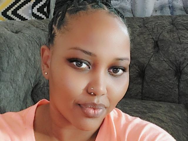 TeeTolia has a cute face with a nose piercing, subtle makeup, and a slightly pouty expression. She's wearing a pink shirt and has braided hair.