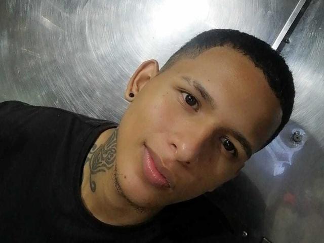 AndresMat ha i capelli corti e scuri, degli orecchini neri, un tatuaggio sul collo e indossa una maglietta nera, con un leggero sorriso. La sua pelle è abbronzata..