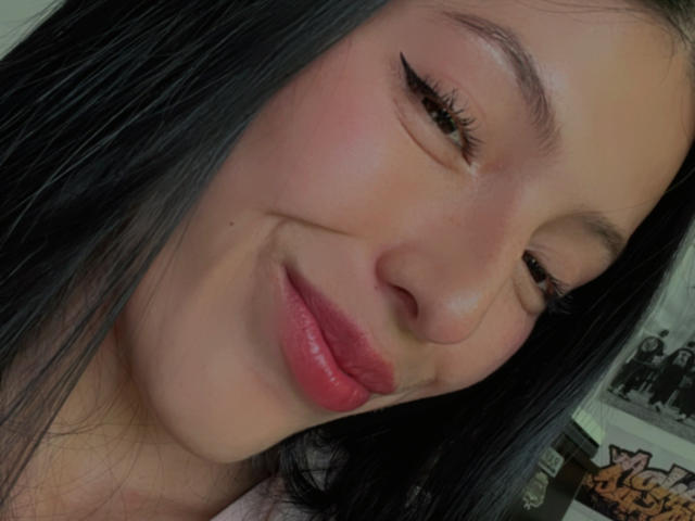 AizenMyoo has a cute smile with red lipstick, black eyeliner, and black hair. Her skin is fair, and she's slightly squinting. She's looking to the right.