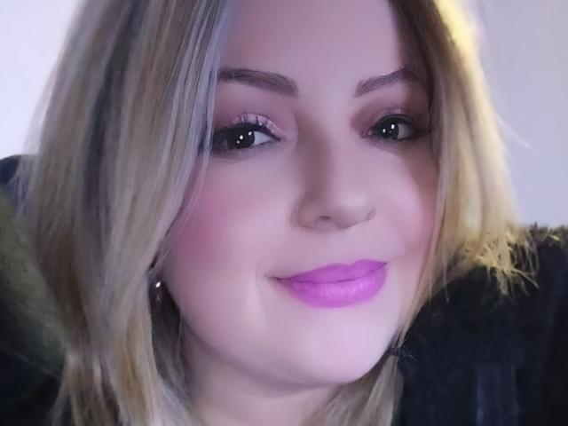 NatalyHami's face, with blonde hair, pinkish blush, purple lipstick, and dark eyebrows, smiling softly. Her tits are not visible, and her ass is not in the image.