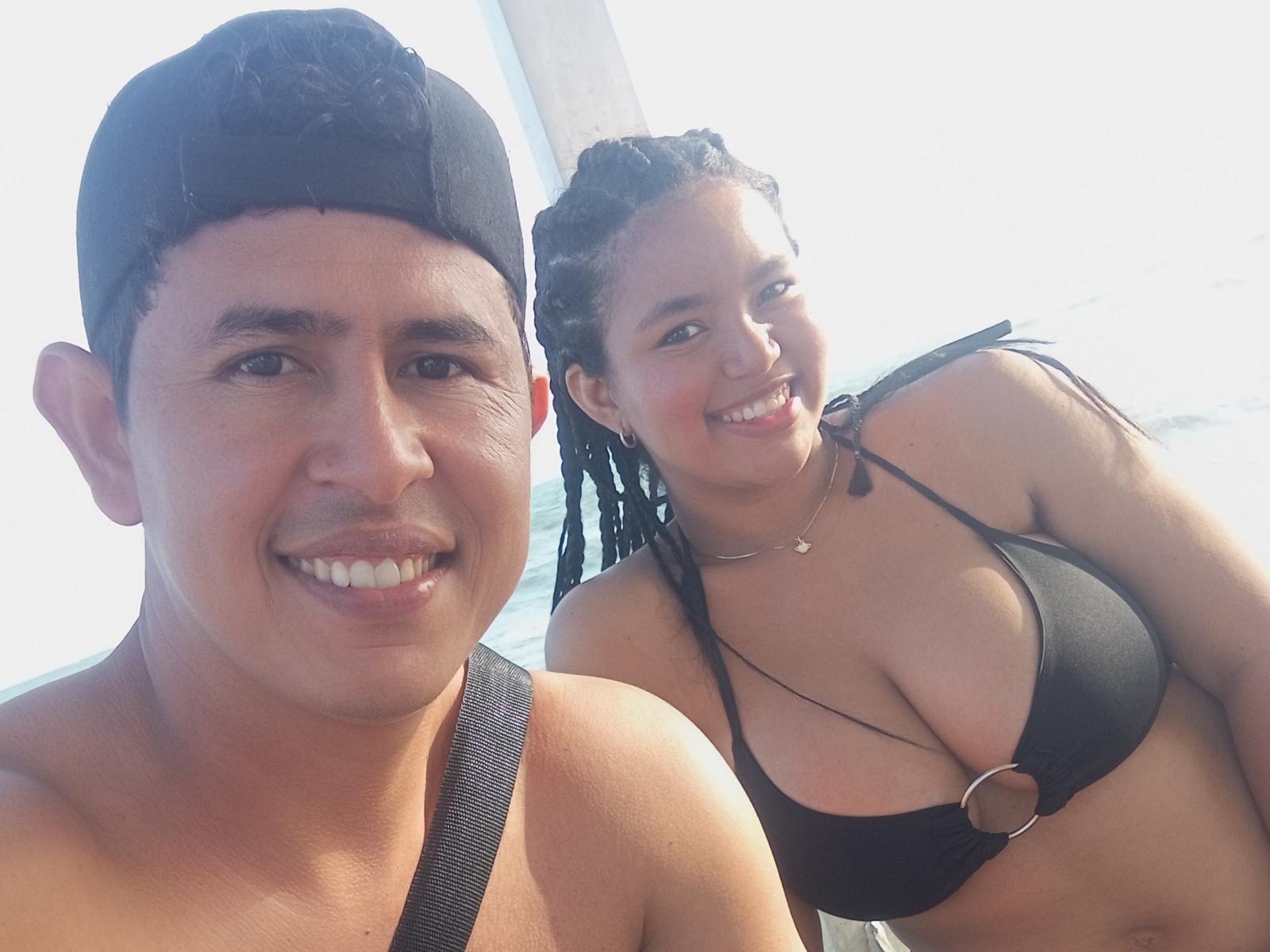 AngelsCouple, a tan dude with a black cap, smiling, and AngelsCouple, a curvy woman with black braids, big tits in a black bikini, smiling on a boat.