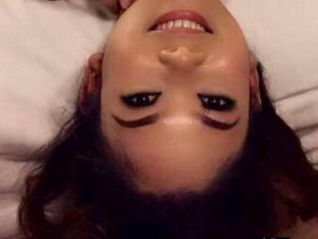 InnocentAne's upside-down face, smiling with dark eyebrows shaped like wings, brown eyes, and red lipstick. She's lying on a white pillow, head in the frame.