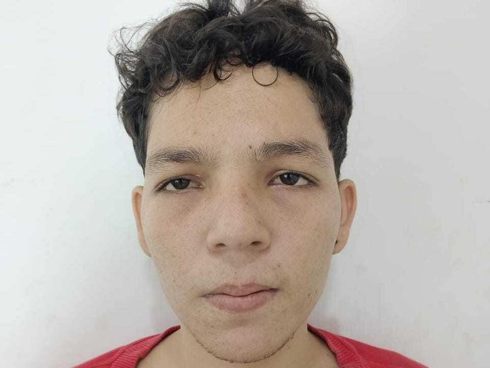 DeivisSexLov has curly dark hair, light brown skin, brown eyes, and a red shirt. His face is slightly freckled with a neutral expression.