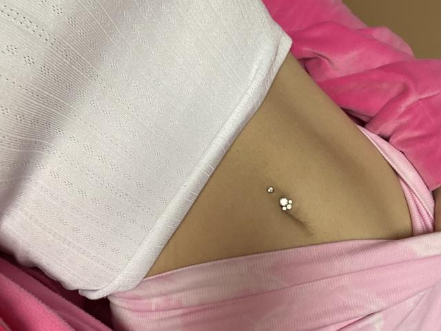 Le ventre plat d'Olieri, teinté de brun, avec un piercing argenté au nombril, portant un haut blanc à rayures, sans manches, et un bas rose, de type "culotte"..