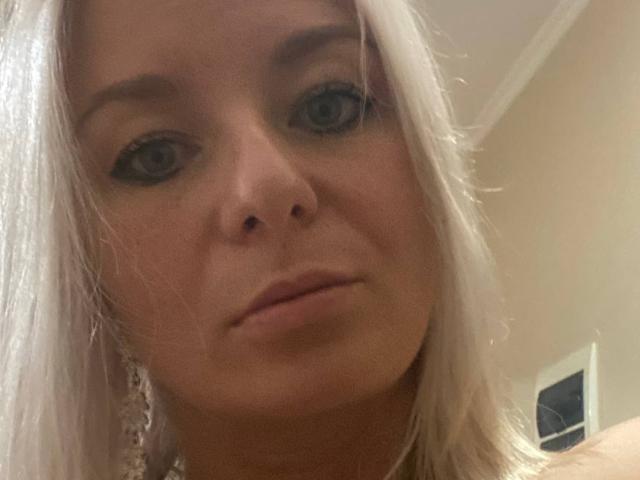 RoseeZ has pale skin, white hair, and dark eyeliner. Her small nose and slightly parted lips are visible. She's wearing a lace earring on the left side.