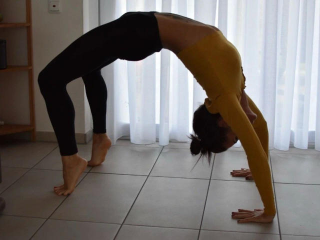 MadameSolenne1-hot buigt voorover in een yoga-houding, haar gele top laat haar rug zien en haar zwarte broek bedekt haar billen. Ze staat op een vloer van witte tegels, met haar handen op de vloer..