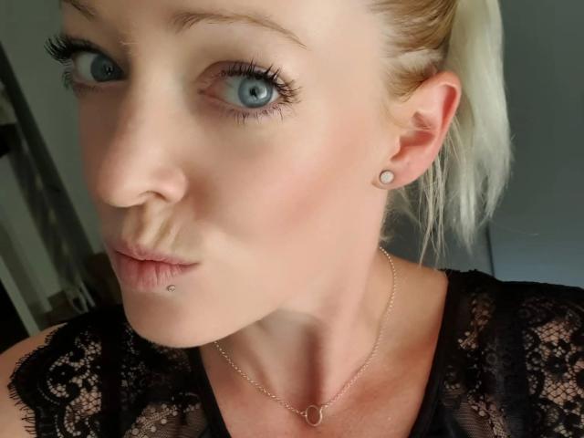 LeaKirsch-hot with pale skin, blue eyes, and blonde hair in a ponytail, wearing black lace, has a lip piercing and small ear studs, and a delicate necklace.