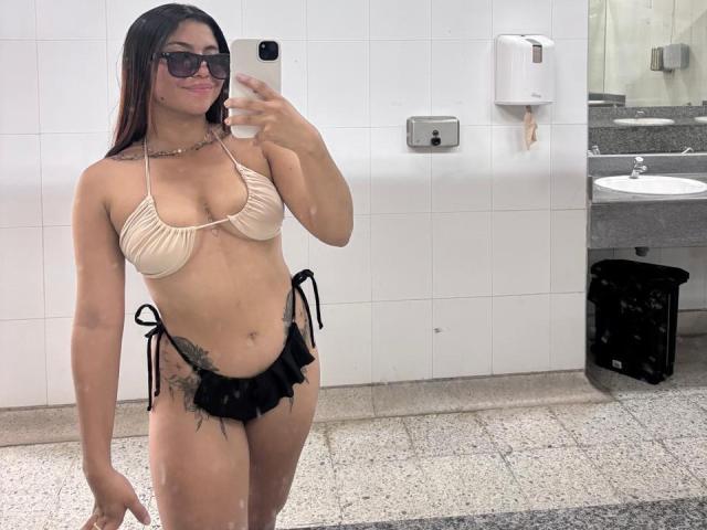 VALERY1CHAARMS in a mirror selfie, wearing a beige bikini top and black ruffle bikini bottom, showing her tits, ass, and a tattoo on her left side.