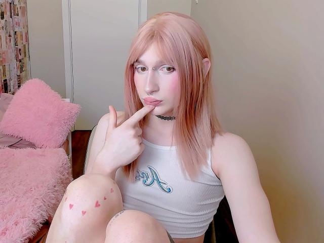 Mika-Candy-hot with pink hair, wearing a white tank top, biting her finger, sitting with knees up, showing pink knee marks, wearing a black choker.