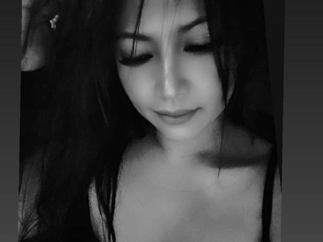 Photo en noir et blanc de Looca29, avec de longs cheveux foncés, les yeux fermés, un léger sourire, et de petites seins, portant un haut sans bretelles, affichant une expression douce et sereine..
