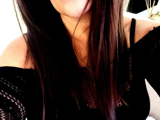 EmmaNlovely's tits, covered in a black lace off-shoulder top, with long brown hair falling over her neck and chest. Her skin is light, and she's partially visible.