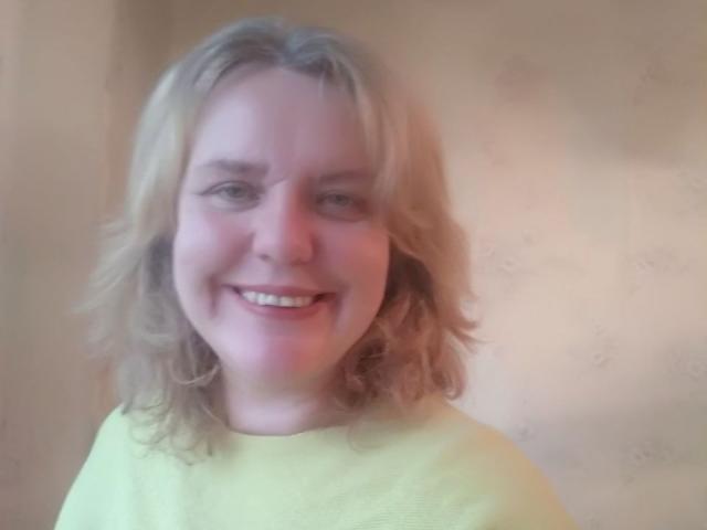 VestaWoody has blonde, wavy hair and a pinkish face, smiling with white teeth. She's wearing a yellow shirt and has a soft, chubby appearance.