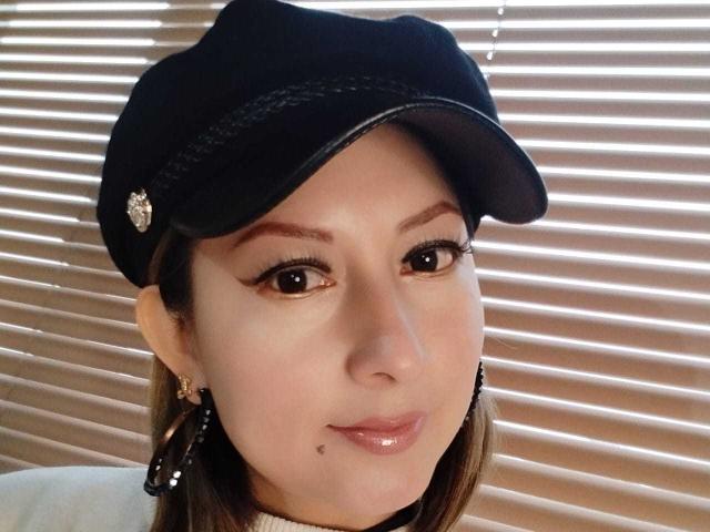 EvellynMiller with dark brown eyes, wearing a black cap, shiny pink lips, small mole on chin, earrings, and light makeup. Her tits are not visible.