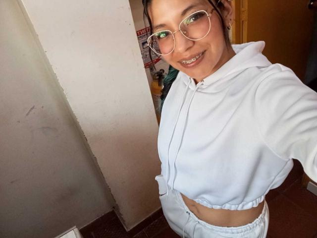 PaulinaColemann with glasses, smiling, wearing a white hoodie and matching pants, showing her midriff, and looking at the camera, standing in a doorway.