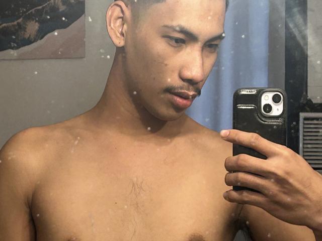 Mirror selfie of HiddenDesireAru, shirtless with light brown skin, short hair, mustache, and small chest hair, holding a black iPhone, looking down at the phone.