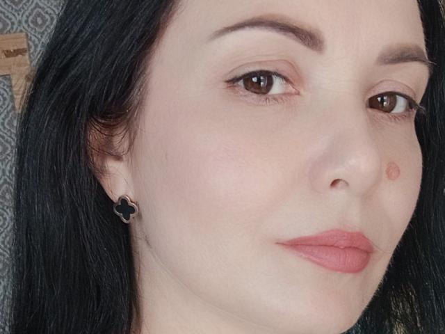 JosefinaWelpo has pale skin, black hair, brown eyes, and pink lipstick with a small red mole on her right cheek. She's wearing black cat-ear earrings.