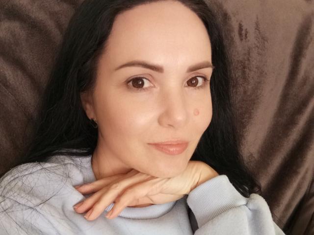 JosefinaWelpo has a cute face with dark hair, brown eyes, and a small beauty mark on her left cheek. She's wearing a light blue sweater, resting her chin on her hand.
