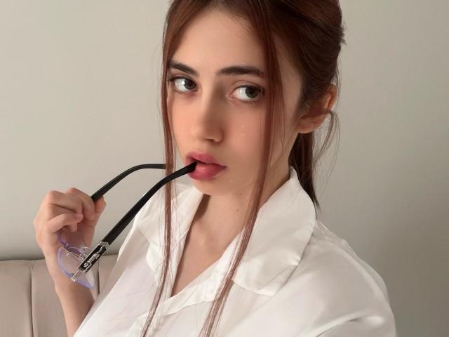 SweetyVikky with brown hair, wearing a white doctor's coat, biting a black stethoscope, has pink lips, and brown eyes, in a softly lit, neutral-colored setting.