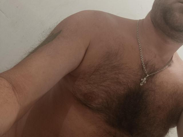Effetto: Il petto peloso di Gerald, con una collana a catena d'argento, capezzoli visibili e una testa leggermente sfocata, mentre si fa un selfie. Un braccio di EffectGerald è parzialmente inquadrato, mostrando un tatuaggio..