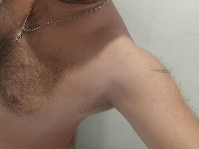 Betonen Sie Gerald's männliche Seite mit einem kleinen Tattoo in der Nähe des Schulters, einer Kette um den Hals und einer sichtbaren Achselhöhle mit etwas Körperbehaarung..