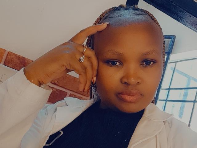 CorrieDee with dark skin, braided hair, wearing a white jacket, black turtleneck, holding phone to ear, ring on finger, serious expression, pouty lips.